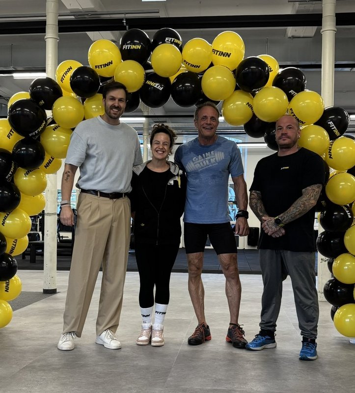 Vier Personen posieren vor einem Ballonbogen mit FITINN-Logo in einem Fitnessstudio in Wien.