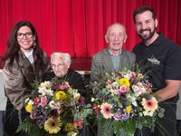 Ehrenamtliche mit Blumensträußen vor rotem Vorhang in Amstetten