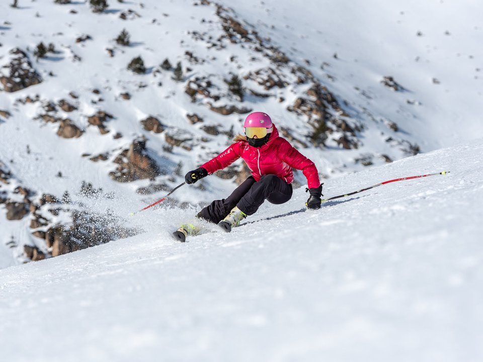 Young blonde woman in ski goggles and helmet skiing on a snowy mountain slope